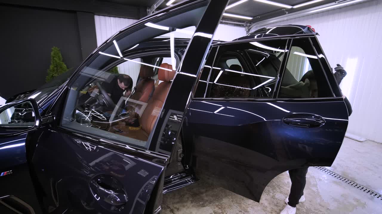 el lavador de coches profesional con guantes negros limpia el coche después de lavar y forrar la cerámica. conceptos de: trabajo profesional, varias herramientas de lavado, limpieza para brillar.