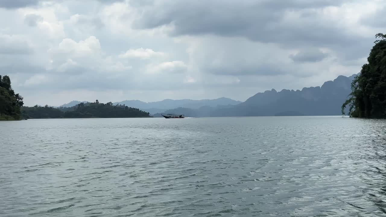 Khao Sok Lake: A boat smoothly traverses the water from right to left, offering a serene spectacle of fluid movement against the lake's scenic backdrop