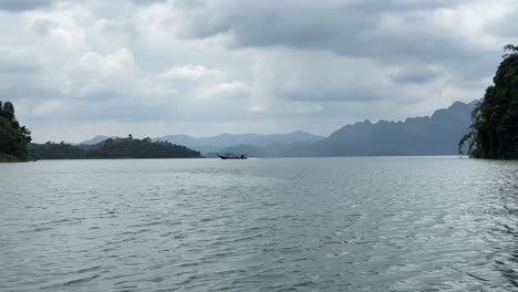 Lago-Khao-Sok:-Un-Barco-Atraviesa-Suavemente-El-Agua-De-Derecha-A-Izquierda,-Ofreciendo-Un-Espectáculo-Sereno-De-Movimiento-Fluido-Con-El-Telón-De-Fondo-Escénico-Del-Lago.