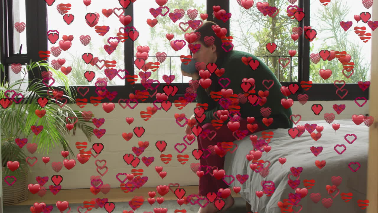 Woman sitting on edge bed in bedroom, with heart emojis floating around marketing campaign