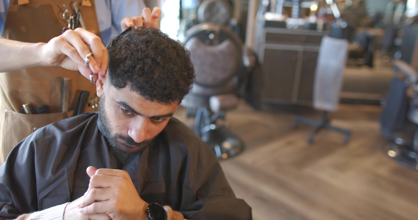 Afroamerikansk mand i barberstol, frisør løfter hår og trimmer linje med saks for at forme