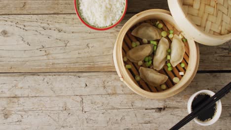 Composition-of-bamboo-steamer-with-gyoza-dumplings-and-soy-sauce-on-wooden-background