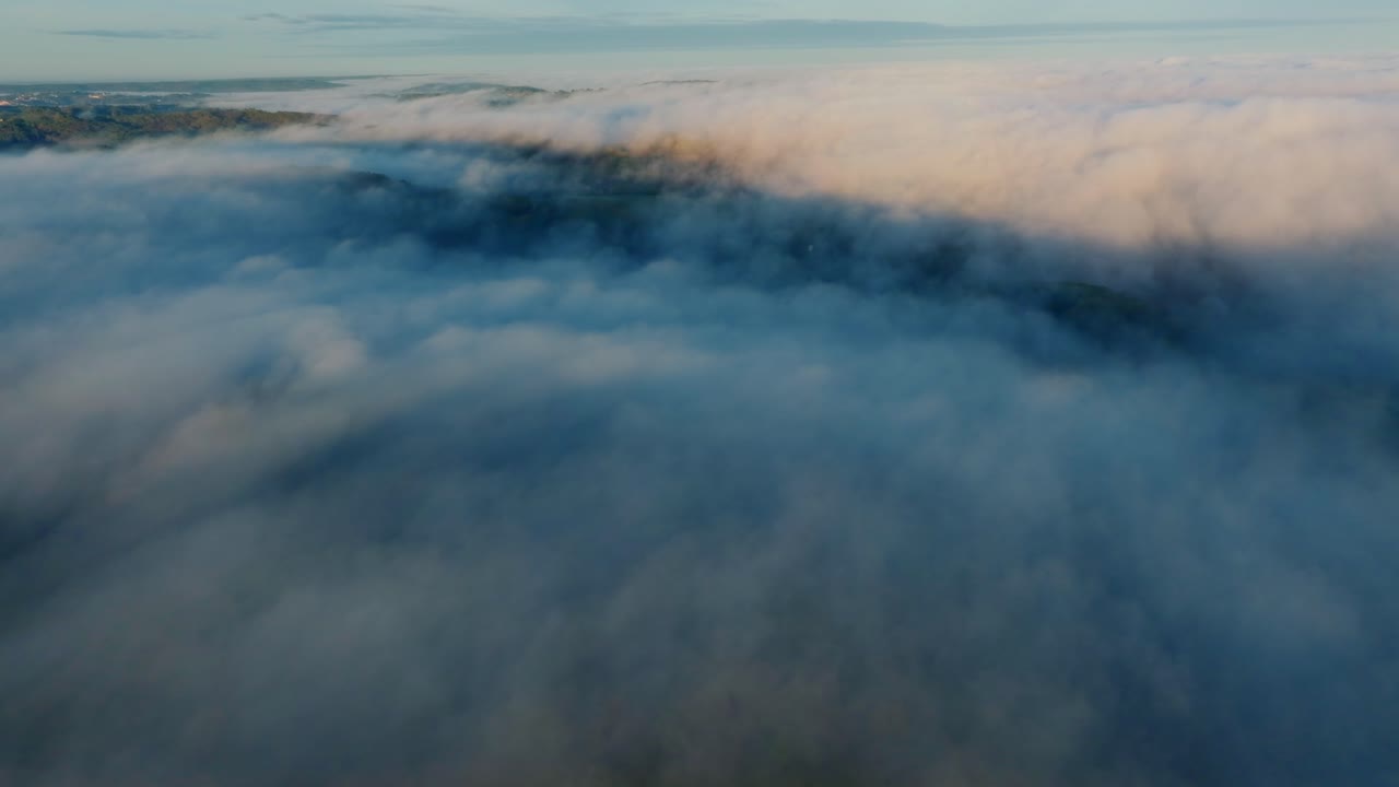 Rolling fog sweeps across rural hills and forests in early morning light.