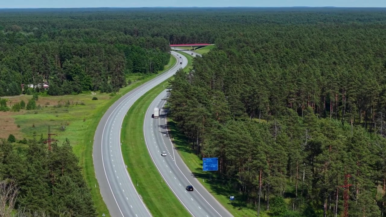 Drone flyver til venstre og afslører en bred udsigt over motorvej, der krydser skove nær Garkalne