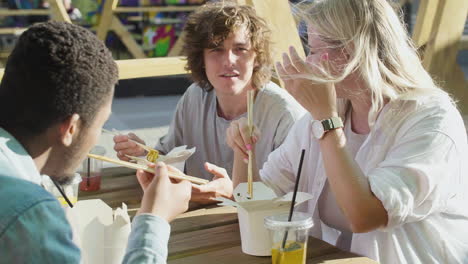 group of  friends sitting around an outdoortable, while eating street food and chatting together