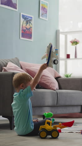 toddler boy plays with airplane while preschooler builds wall from colorful constructor blocks. girl enjoys creative activity sitting on floor with brother