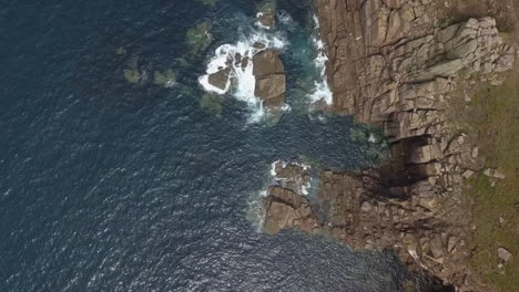 vertical aerial over rugged stone ocean cliffs, waves crash on rocks