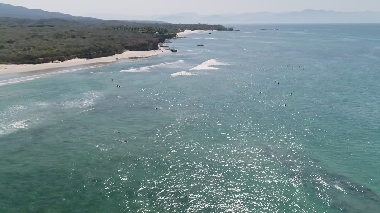 Ampia ripresa aerea che circonda un gruppo di surfisti in acqua blu in attesa delle onde, 4K