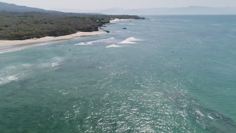 Wide-aerial-circling-group-of-surfers-in-blue-water-waiting-for-waves,-4K