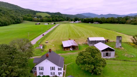 aerial along long roadway with farmhouse as car drives into the distance near mountain city tennessee