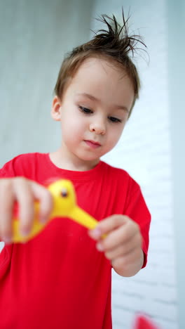 baby boy wearing long red t-shirt closes the balcony door. happy child comes up to a desk to play with toys. low angle view. vertical video.
