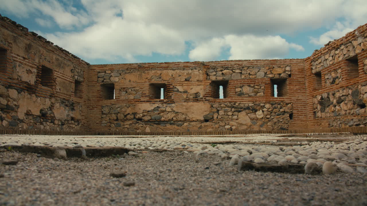 Ground-level shot inside old Spanish fortress shows textured stone and brick walls with defensive slits under dramatic cloudy sky