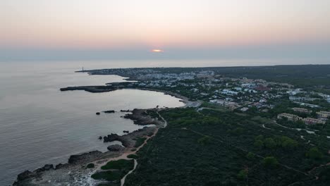 Drone shot of a sunset and a small village by the coast and a lighthouse. On Menorca, Spain, Mediterranean sea.