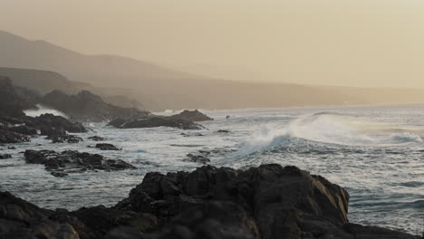 costa rocosa del océano con olas salpicando rocas y cielo naranja en el fondo