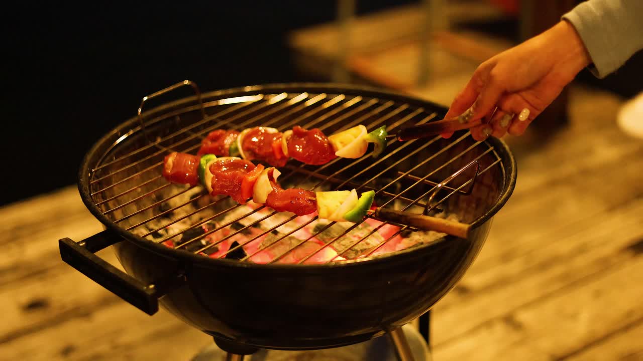 Hands preparing skewers on a charcoal grill