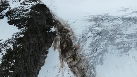 Vista-Aérea-Que-Captura-Caídas-De-Piedra-Sobre-La-Superficie-De-Un-Glaciar-En-Hohe-Tauern,-Yuxtaponiendo-Piedra-En-Bruto-Contra-Suaves-Extensiones-Heladas