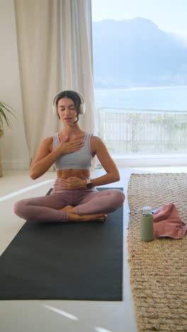 vertical video: meditating at home, woman in headphones practicing mindfulness on yoga mat