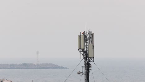 antena de torre de red celular de pie en la costa del mar con paisaje marino en el fondo de la niebla