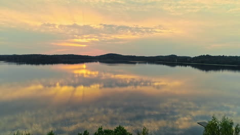 aerial view of calm reflective lake with orange sunset rays and clouds