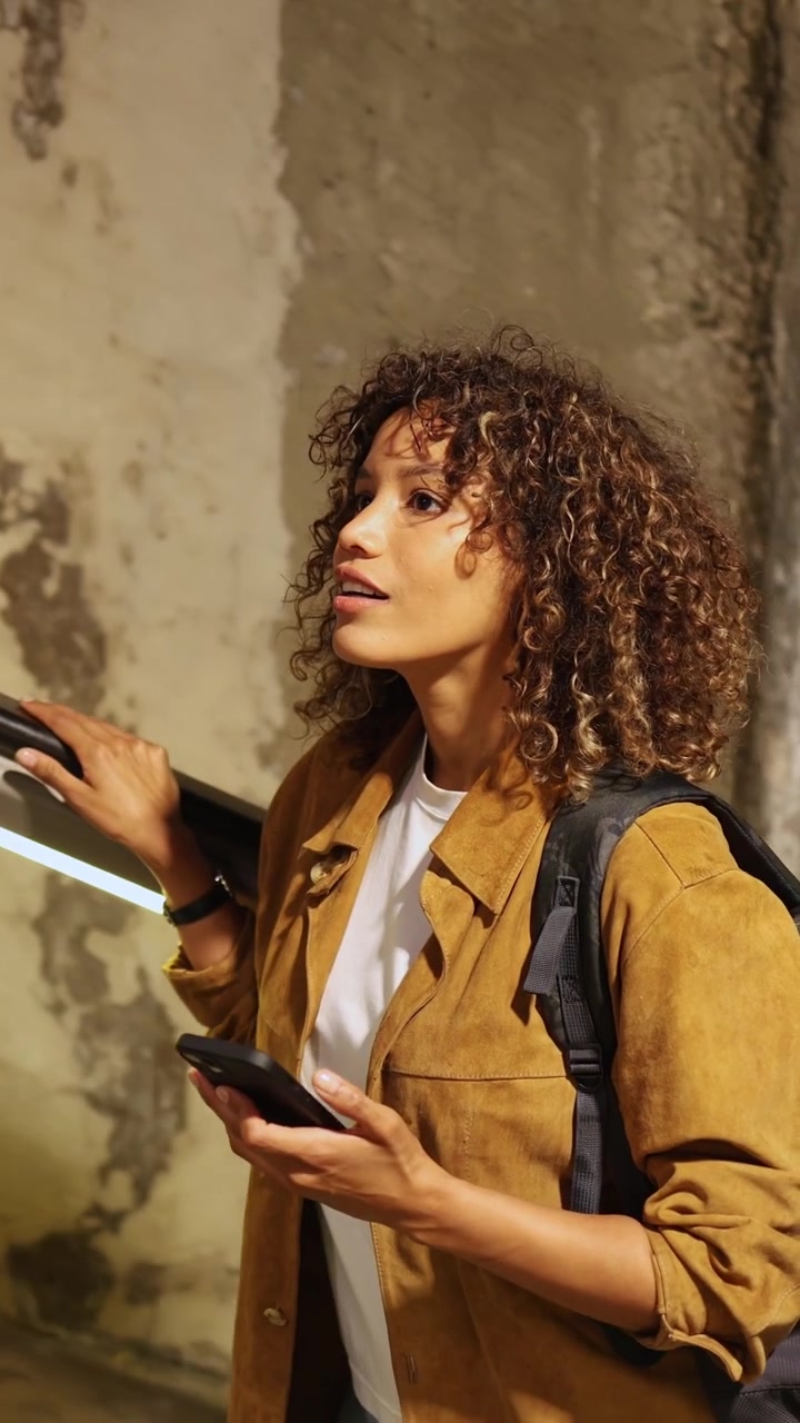 Young Woman with Curly Hair Riding Escalator and Using Smartphone