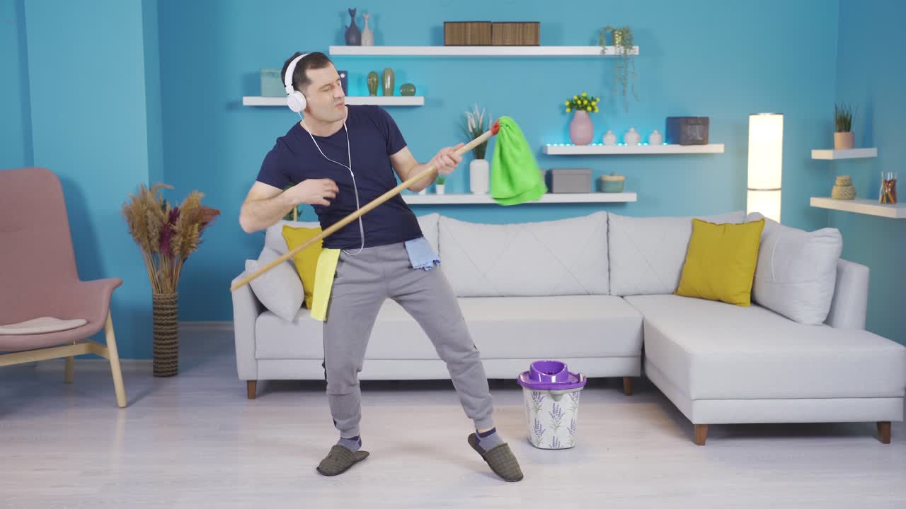 el hombre que se sumerge en la música que escucha mientras limpia su casa y comienza a bailar y hacer movimientos divertidos.