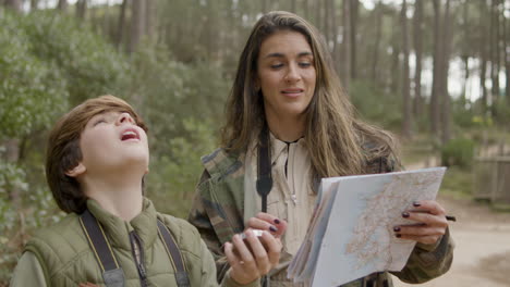 caucasian woman and her son navigating in the forest with the help of map and compass