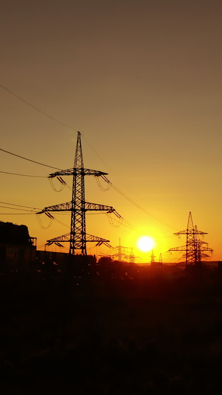 Industrial zone at sunset. High-voltage electric lines near factory with pipes with dirty smoke in the evening. Dark silhouettes of power station. Vertical video