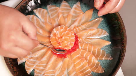 putting roe to a platter of salmon sashimi in a sushi restaurant - overhead shot