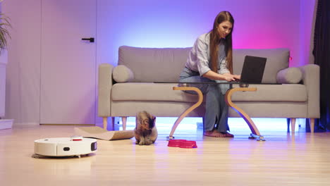 mujer trabajando desde casa con gato y aspirador robótico