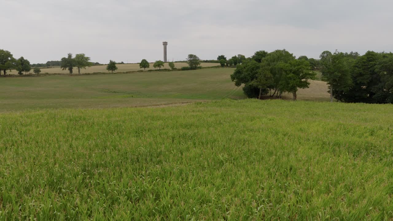 Aerial drone view of wide green fields, farmland, and scattered trees stretching into the countryside beneath an overcast sky