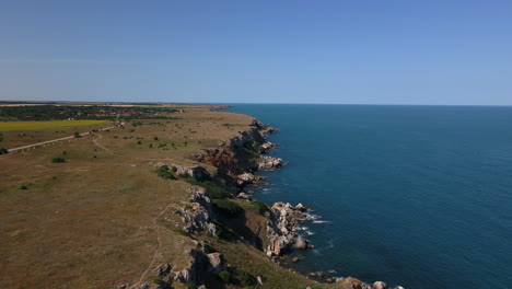 A-drone-shot-of-rocky-mountainous-coast-with-green-trees-and-blue-sea-with-white-foaming-waves