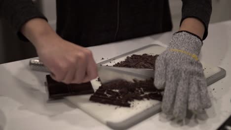una niña corta chocolate negro antes de derretirlo para hacer galletas de mantequilla millonarias mientras usa guantes de seguridad-7