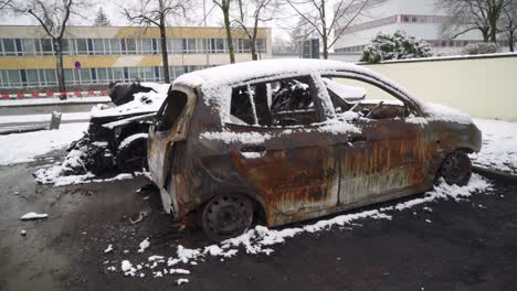 burnt-out car arson vandalism on city street, vehicle covered in snow