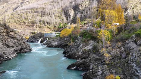 drone footage captures the kawarau river's turquoise waters and surrounding autumn foliage near a hydroelectric power station in queenstown, new zealand