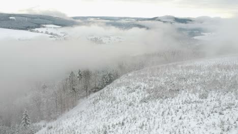 aerial dolly out snowy landscape hills pine trees fog clouds valley