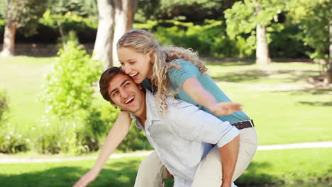 A-man-gives-his-girlfriend-a-piggyback-as-they-look-at-the-camera-and-smile