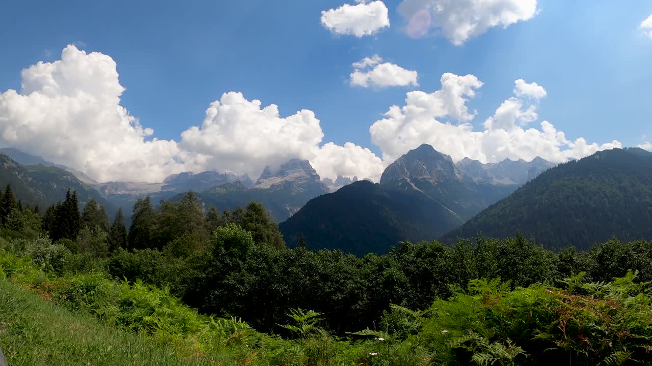 Beautiful view of lush green forest and mountain range under bright blue sky with scattered clouds in Scotland, showing peaceful natural landscape and vibrant summer colors in daylight.