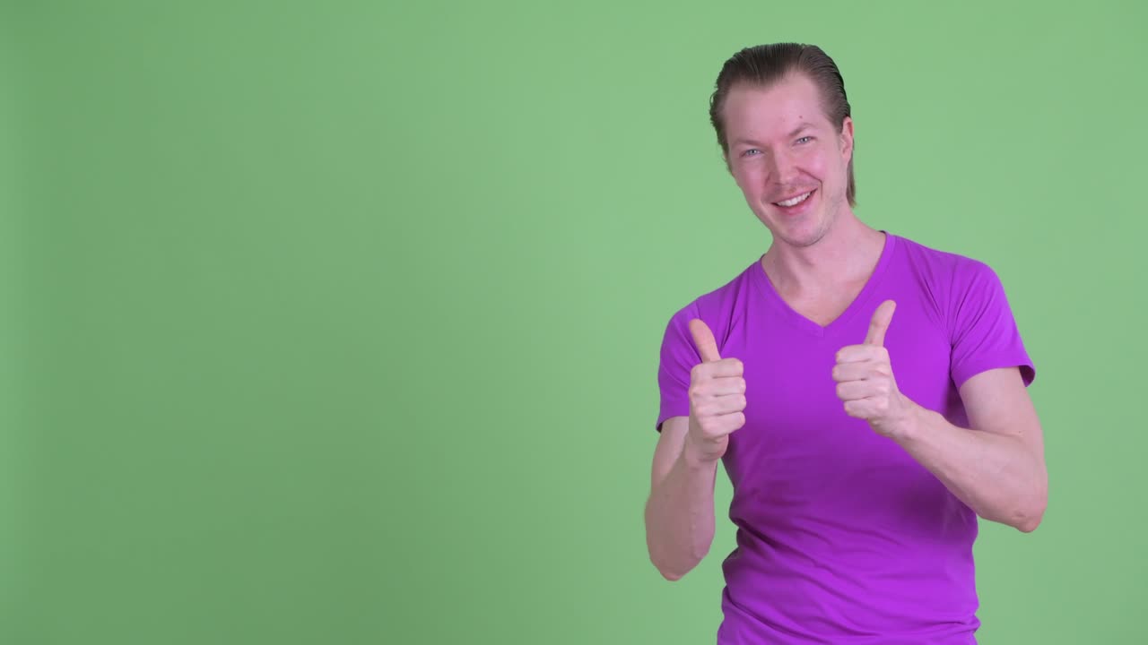 fotografía de estudio de un joven mostrando el espacio de copia y sonriendo mientras levanta los pulgares contra el fondo verde