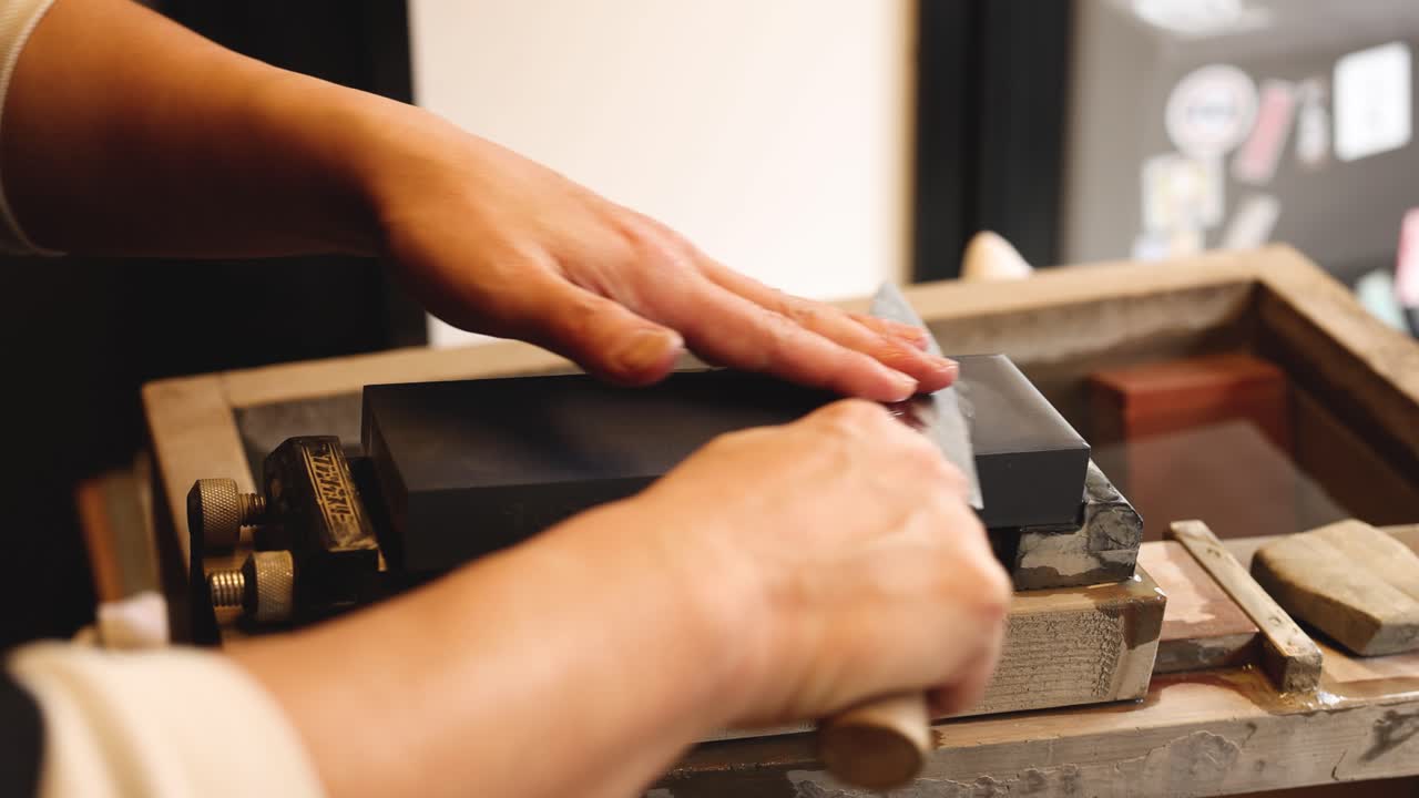 Hands skillfully sharpening a knife on a stone.