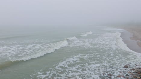 aerial establishing view of port of liepaja concrete pier, baltic sea coastline , foggy day with dense mist, moody feeling, big storm waves splashing, wide drone shot moving forward low