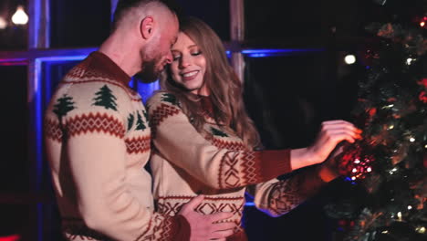 young family decorates christmas tree. cheerful girl is hanging christmas ball. couple in love prepare house for new year holidays