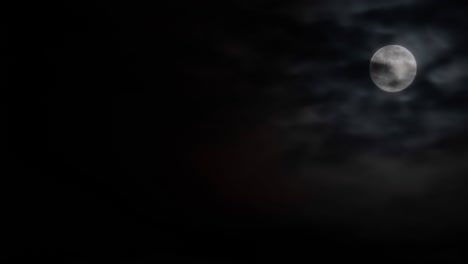 timelapse - full moon rising against black sky with moving clouds at night