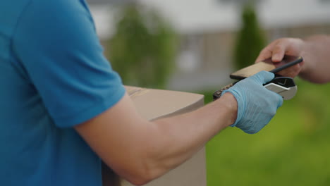 delivery hand of young man pays for purchases using the contactless payment nfs system. young delivery man hold package man client paying by phone for parcel transporting payment uniform express order