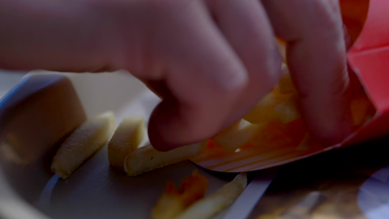 cerca de papas fritas en un recipiente en una bandeja, una mano caucásica entra y agarra unas papas fritas listas para comer esta comida para el almuerzo.