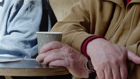 ancianos amigos sentados en un banco del parque mesa bebiendo café taza café hablando discutiendo discutir hablar recuerdos cerrar manos mano conversación conversando sentado paciencia esperando restaurante