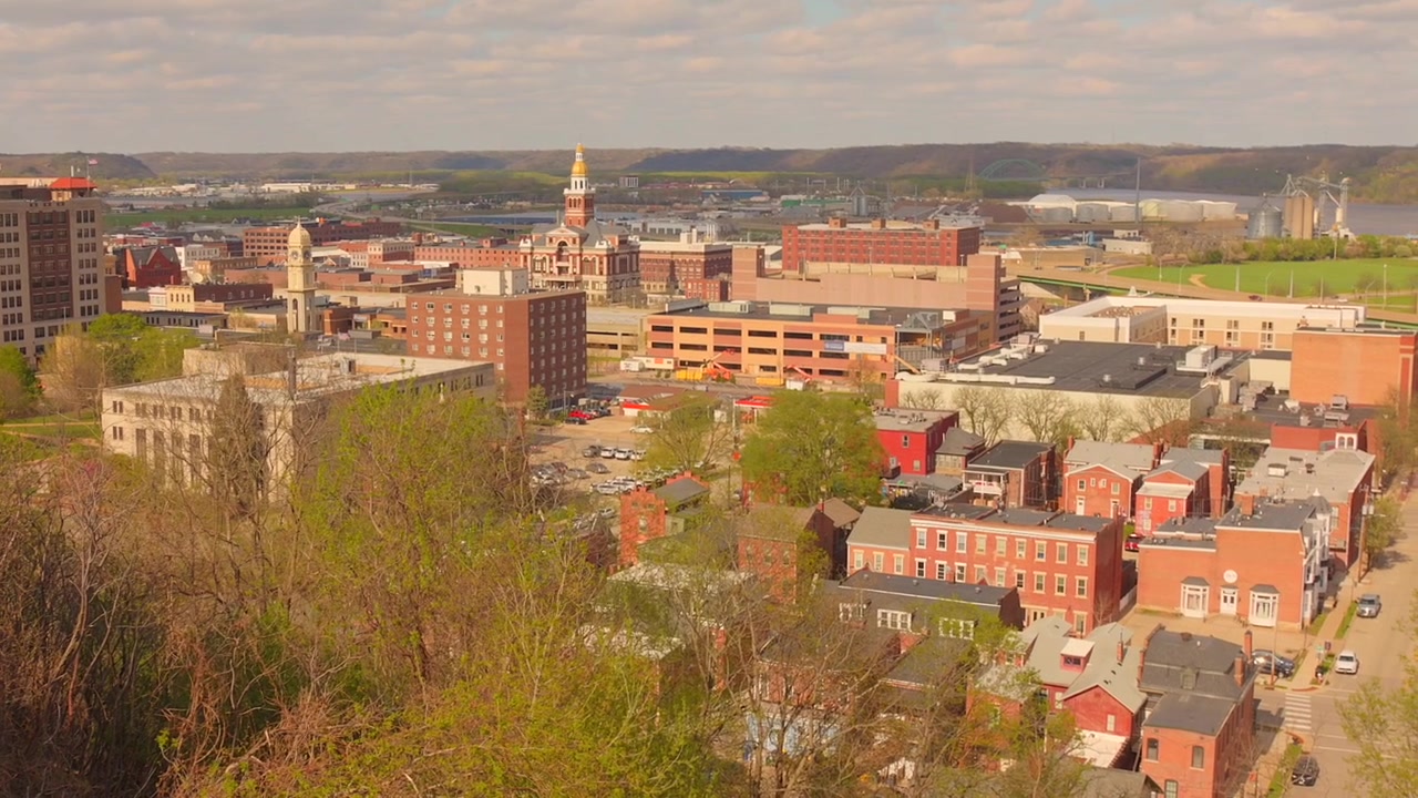 Bredt panoramisk luftfoto av bybildet og sentrums silhuett av Dubuque, Iowa, med historiske mursteinsbygninger, urban arkitektur og bølgende åser i bakgrunnen på en lys dag