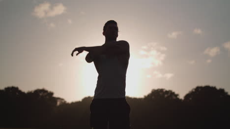 young attract man stretches in park before he goes for a run with the evening sun in the background