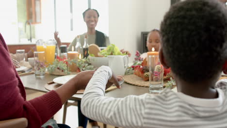 happy african american multi generation family holding hands at thanksgiving dinner, slow motion