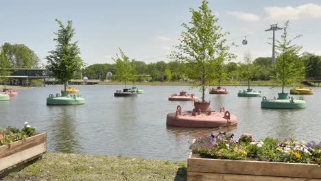 panoramic shot of trees growing in metal containers floating in a park pond with a moving cable cars in the background