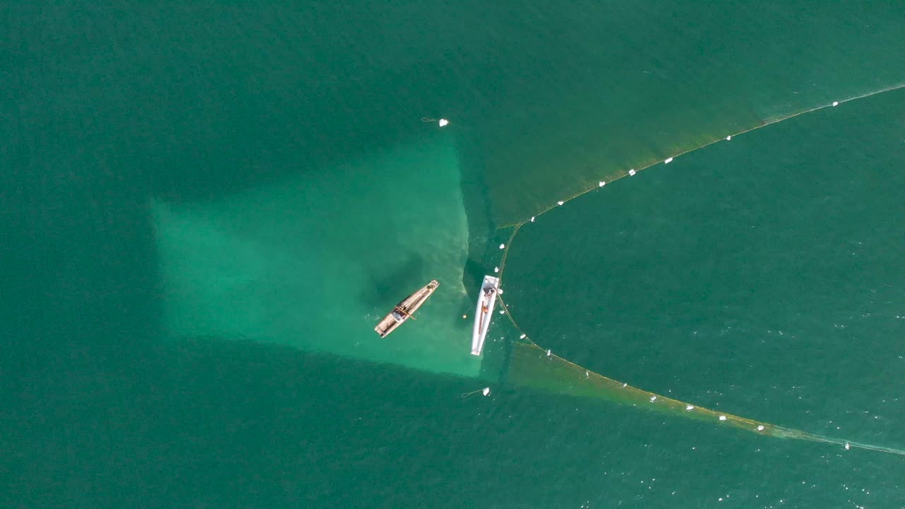 바다의 수면 위로 물고기를 잡기 위해 그물 덫을 놓는 어부의 공중 하향식 전망